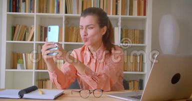 年轻有魅力的女商<strong>人坐</strong>在笔记本<strong>电脑前</strong>摆姿势在手机上自拍的特写
