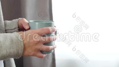 女孩喝一杯热茶或咖啡。 女人`手拿着一个杯子，杯子上有蒸汽