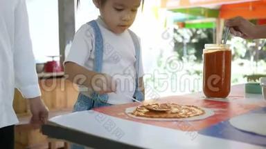 快乐的孩子们在厨房准备自制披萨。 小女孩正在用勺子涂抹番茄酱和面粉揉成的披萨。 家庭娱乐