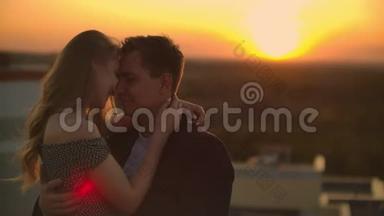 拥抱站在屋顶日落。 日落时的夏季屋顶。 一个男人和一个女孩在屋顶上进行了一次浪漫的约会
