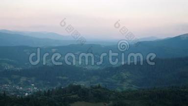 山谷中的村庄在绿松树之间，黄昏时分，地平线上有夕阳。 喀尔巴阡山脉夏季。 美丽的m