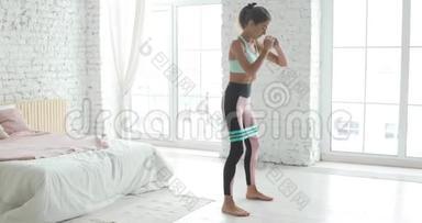 女孩正在做蹲臀部使用<strong>拉伸</strong>带，锻炼训练在家里。