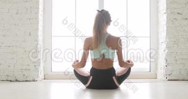女子正在家中冥想莲花姿势，靠近窗户后瑜伽，后景。