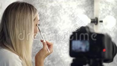 漂亮的金发化妆师正在用眼影照镜子