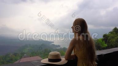 一个穿着黄色衣服和帽子的年轻女子参观了一个观点，在巴图尔山上看到了一个风景，它`隐藏在里面的卡尔德拉