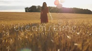 棕色头发的年轻女子手里拿着气球穿过金色的麦田。 穿着红裙子的漂亮女孩