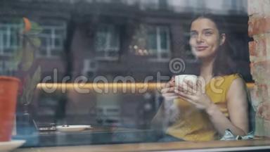 快乐的年轻女士喝<strong>着</strong>咖啡<strong>看着窗外</strong>独自坐在咖啡馆里