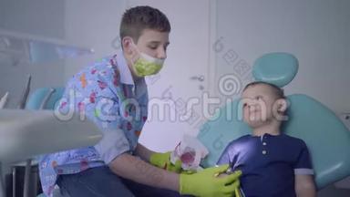 十几岁的男孩戴着医用口罩和手套，小孩子在牙医办公室玩耍。 年轻人教孩子刷牙