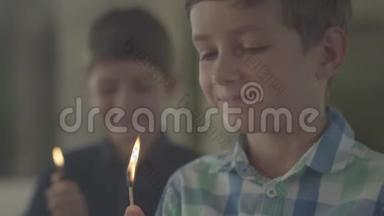 两个可爱的兄弟在黑暗的烟雾弥漫的房间里带着火。 一个男孩在背景中点燃打火机，另一个男孩在背景中点燃火柴