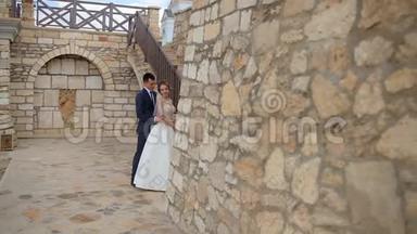 一对年轻夫妇在一座漂亮的城堡和石墙旁边摆姿势拍照，石墙上有一个石楼梯