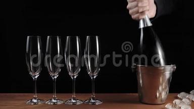 好香槟酒。 四个空杯子，香槟酒立在木桌上，背景黑色。 手拿瓶香槟