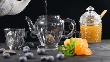 茶叶酿造。 绿色中国茶花玻璃茶点在木制背景。 蓝莓，玻璃罐加蜂蜜。 浇注