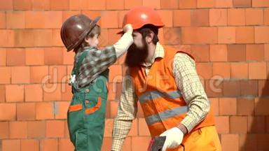 小儿子<strong>工人</strong>竖起砖墙。 戴着安全帽的儿子帮助他的<strong>父亲</strong>。 父子一起建房子。 儿子