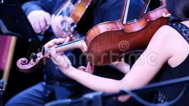 在古典音乐交响乐团演奏时，女演奏小提琴。 背景中的小提琴人。 最后报告