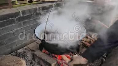在火上面的大锅里煮排骨。 蒸汽和气味在盖子下面留下。 那个人把木头放好