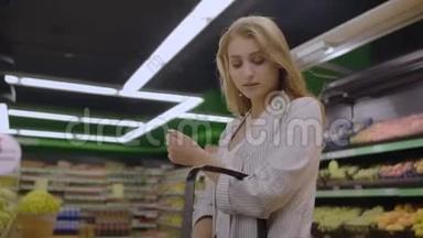 年轻女子称电子秤苹果。 在水果和蔬菜部的超市购物