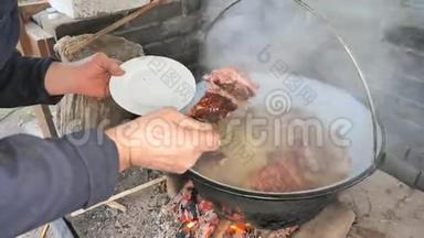 厨师用叉子和盘子从蒸锅里取出煮熟的排骨。 为聚会烹制传统熟食