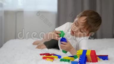 快乐男孩躺在床上，玩着建造者的彩色积木，从它<strong>中建</strong>造出来。
