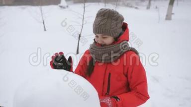 少女在街上玩冬天。 女孩雕刻雪人雪。