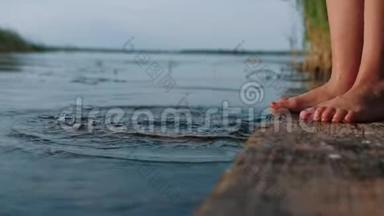 站在湖边古老的木墩上的小女孩把脚浸入水中