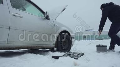 人类在冬天从积雪覆盖的地面上举起汽车电池，并把它带到汽车上。 一次修理或修理