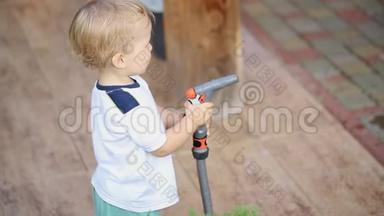 可爱可爱的白种人金发幼儿男孩，玩着帮助父母用软管和喷头给花园和草坪浇水