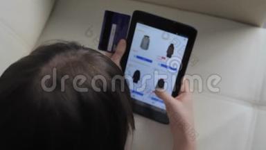 女孩用数字平板电脑制作网上销售购物概念。 黑发女人躺在沙发上看着网上商店付钱