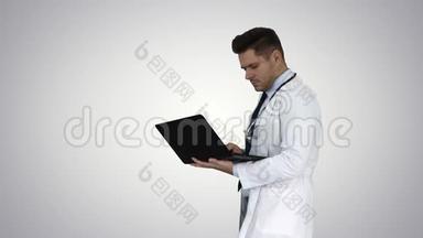 穿着白<strong>色</strong>医用外套和听诊器的人在<strong>渐变背景</strong>下带笔记本电脑行走。