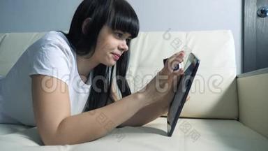 女孩用数字平板电脑制作<strong>网上</strong>销售购物概念。 黑发女人躺在沙发上看着<strong>网上</strong>商店，通过支付