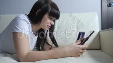 女孩用数字平板电脑制作网上销售购物概念。 黑发女人躺在沙发上看着网上商店的生活方式