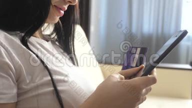 女孩用笔记本电脑数字平板电脑制作网上销售购物概念。 黑发女人躺在沙发上看着网上支付的商店