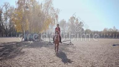 年轻的白种人女孩穿着粉红色的衣服，戴着骑马头盔，在优雅的棕色马身上跳过障碍，骑着马走了