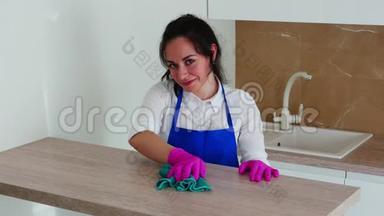 一个黑发女孩正在清洁和微笑的相机。 搓一桌轻木.. 用于清洁的粉红色手套。