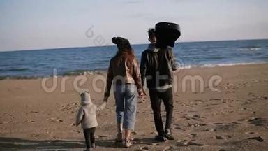 一家人在海滩上散步。父母带着他们的小女儿或太阳沿着海滨散步。他们手牵手。他们是