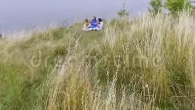 在湖边或河边坐着三个穿着夏日长礼服的女朋友的空中观景。 两个高加索人和一个