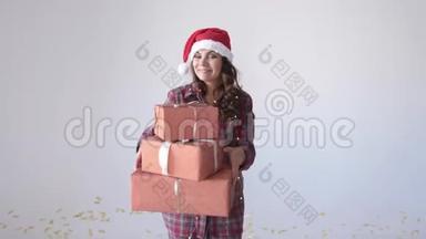 年轻快乐的女人戴着圣诞帽，手里拿着白色背景的礼品盒跳舞。 假期概念
