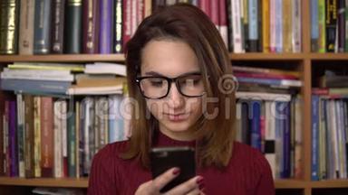 一个年轻的女人正在图书馆<strong>看</strong>智能<strong>手机</strong>。 戴眼镜的女人仔细地<strong>看</strong>着<strong>手机</strong>特写。 在里面