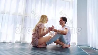 放<strong>大年</strong>轻夫妇坐在地板上，在早晨的阳光下牵手