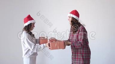 穿着圣诞帽和睡衣的快乐女人给对方一个礼物，摇动礼盒。 假日概念。 慢动作