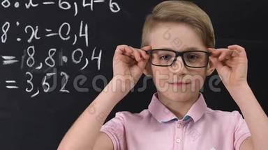 戴眼镜的小学生看着照相机，黑板上写着数学方程式