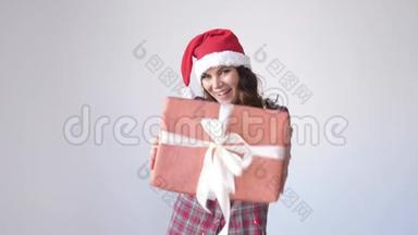 戴圣诞帽的快乐女孩在白色背景上赠送一个礼品盒。 女人手里的小礼物。 假日包装