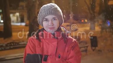 美丽的快乐女孩在夜间冬天的城市吹雪的肖像，女人看着镜头。