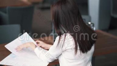 背面，女孩自由职业者看菜单在咖啡馆，笔记本电脑在桌子上，慢动作
