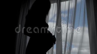 怀孕妇女的剪影抚摸着窗户，抚摸着肚子