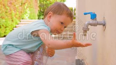 小女孩在玩水。 幼儿玩水从水龙头流出.. 小孩拿着空的塑料瓶