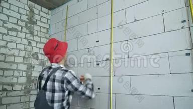 建筑工人在工作中的磨损和红帽将施工夹插入砌块墙中