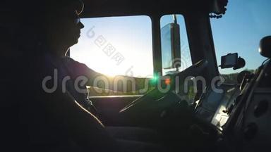 卡车司机晚上开车穿过乡村的剪影。 戴墨镜的人控制着卡车