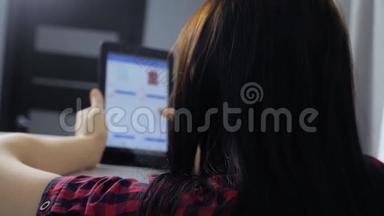 网上购物的概念。 坐在网上商店看商品的年轻女孩在数字平板电脑上购物。 妇女