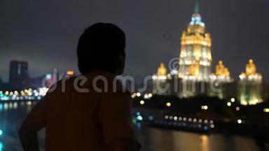 成功的年轻人站在阳台的城市天际线上，莫斯科，夜晚用美丽的波克看着城市的景色