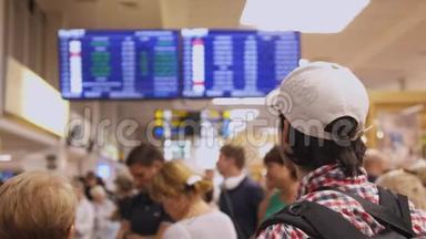 背包旅客在国际机场到达大厅内查看数字航班时刻表显示的航班信息。